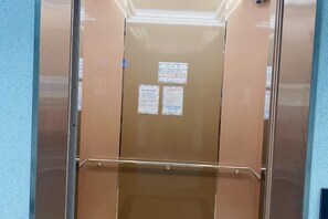 Un ascenseur doté d’un intérieur métallique et de portes en verre, avec deux panneaux d’information fixés au mur.