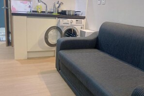A compact living space with a sofa, a washing machine, and a kitchenette. - Jeju (Shinjeju) House (Jeju City)