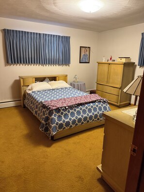 Une chambre à coucher comprenant un lit, une table de chevet, une commode et une étagère fixée au mur.