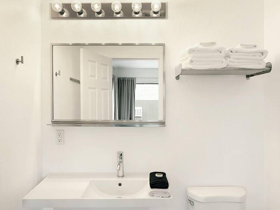 A bathroom with a white sink, a mirror, a toilet, and a towel rack with folded towels.