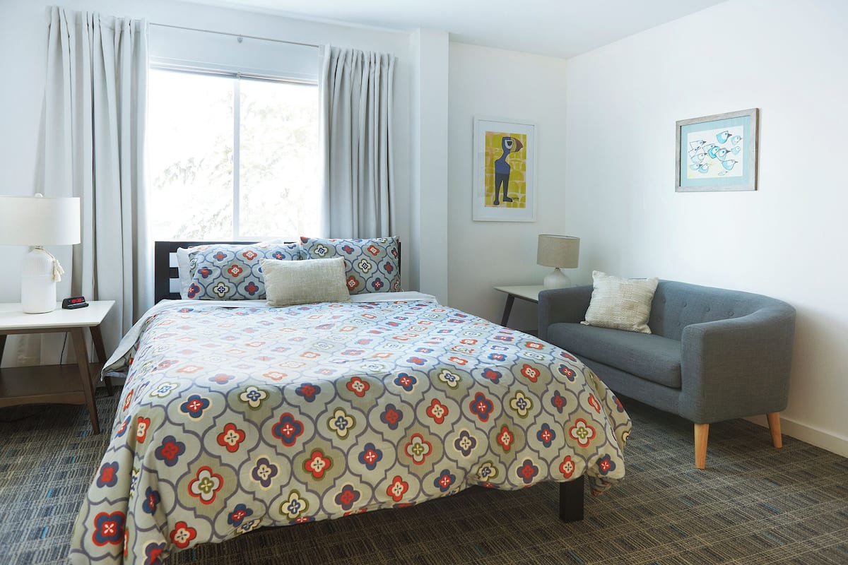 Una camera da letto con un letto, un divano grigio, un tavolino e due lampade a parete.