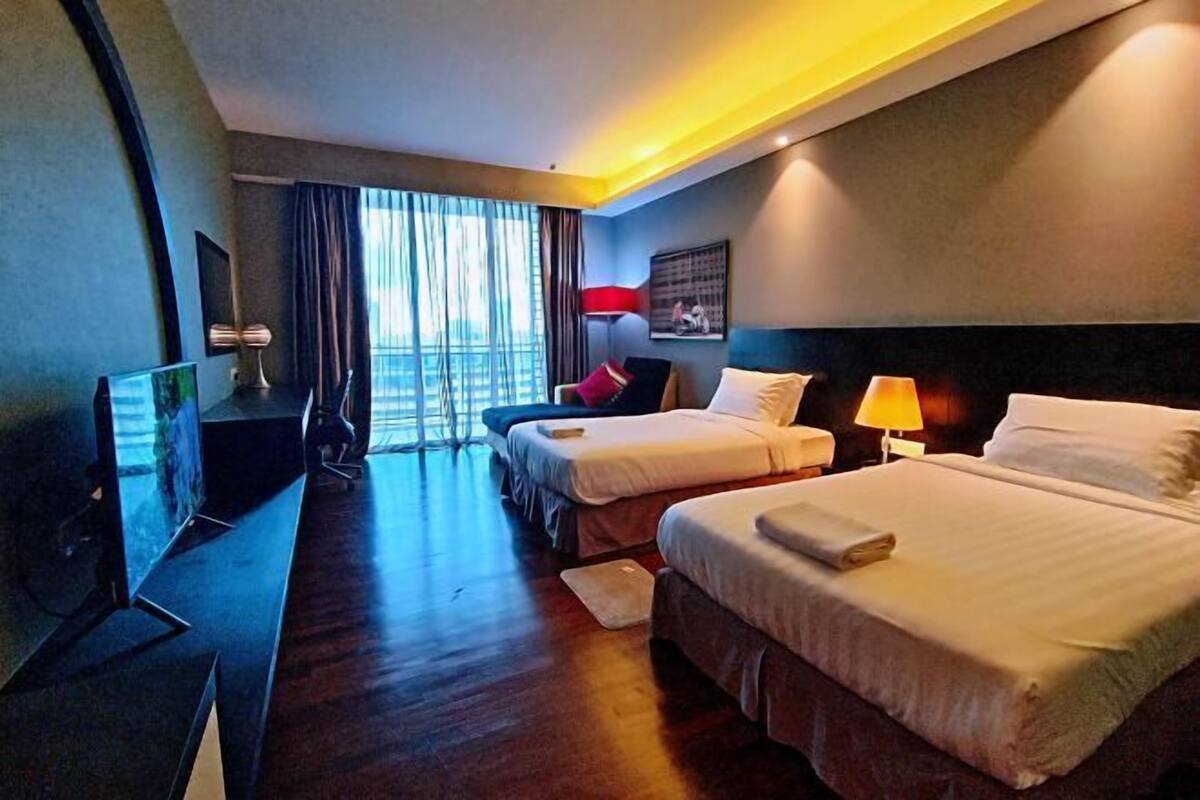 Habitación de hotel con dos camas, un escritorio, un televisor y un amplio ventanal con cortinas.