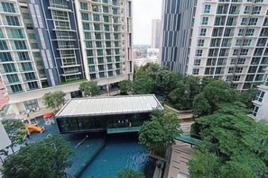 Un edificio residencial alto con piscina en la azotea y abundante vegetación circundante.