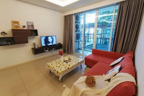 Een woonkamer met een rode bank, een salontafel, een televisie en een balkon met gordijnen.
