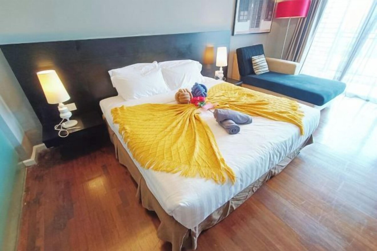 Une chambre d’hôtel avec un lit, une table de chevet avec une lampe, une chaise et une fenêtre.