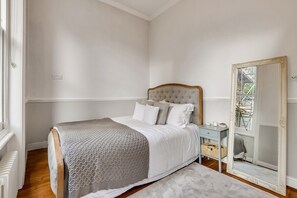 Classic bedroom with a neatly made bed, wooden headboard, and ornate mirror.