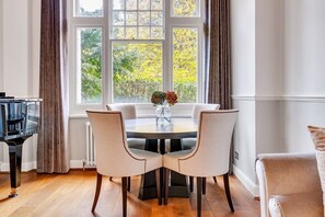 Enjoy meals in this elegant dining area with a round table and four chairs, surrounded by large windows offering a serene view of the outdoors.