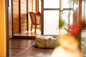 Un interior japonès tradicional amb portes corredisses, una banca de pedra i una cadira amb coixí vermell.