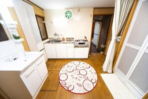 A compact kitchen with white cabinets, a central island, a small sink, and a clock on the wall. - Awaji Seaside Hotel in Ikuho (Awaji City)