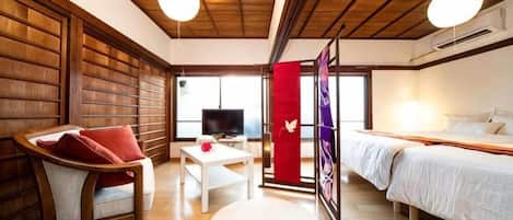 A room with a bed, a TV, a chair, and a table.