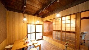 Ein traditioneller japanischer Raum mit Holzwänden und Tatami-Böden, einem niedrigen Tisch mit Kissen und verschiebbaren Türen.