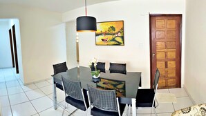 Un coin repas avec une table en verre, des chaises noires, un luminaire suspendu et un tableau au mur.