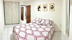 Une chambre à coucher avec un lit, une armoire et une porte qui donne sur une autre pièce. Il y a trois tableaux encadrés accrochés au mur.