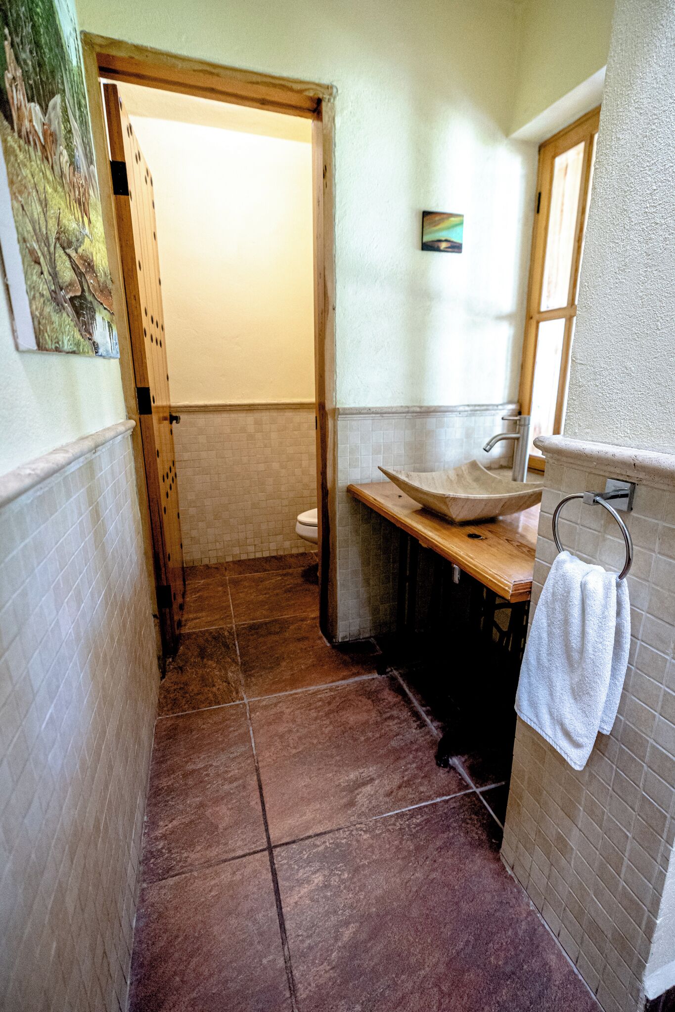 Ein Badezimmer mit Holztür, einem Waschbecken mit Holzablage und einem Handtuch an einem Metallregal.