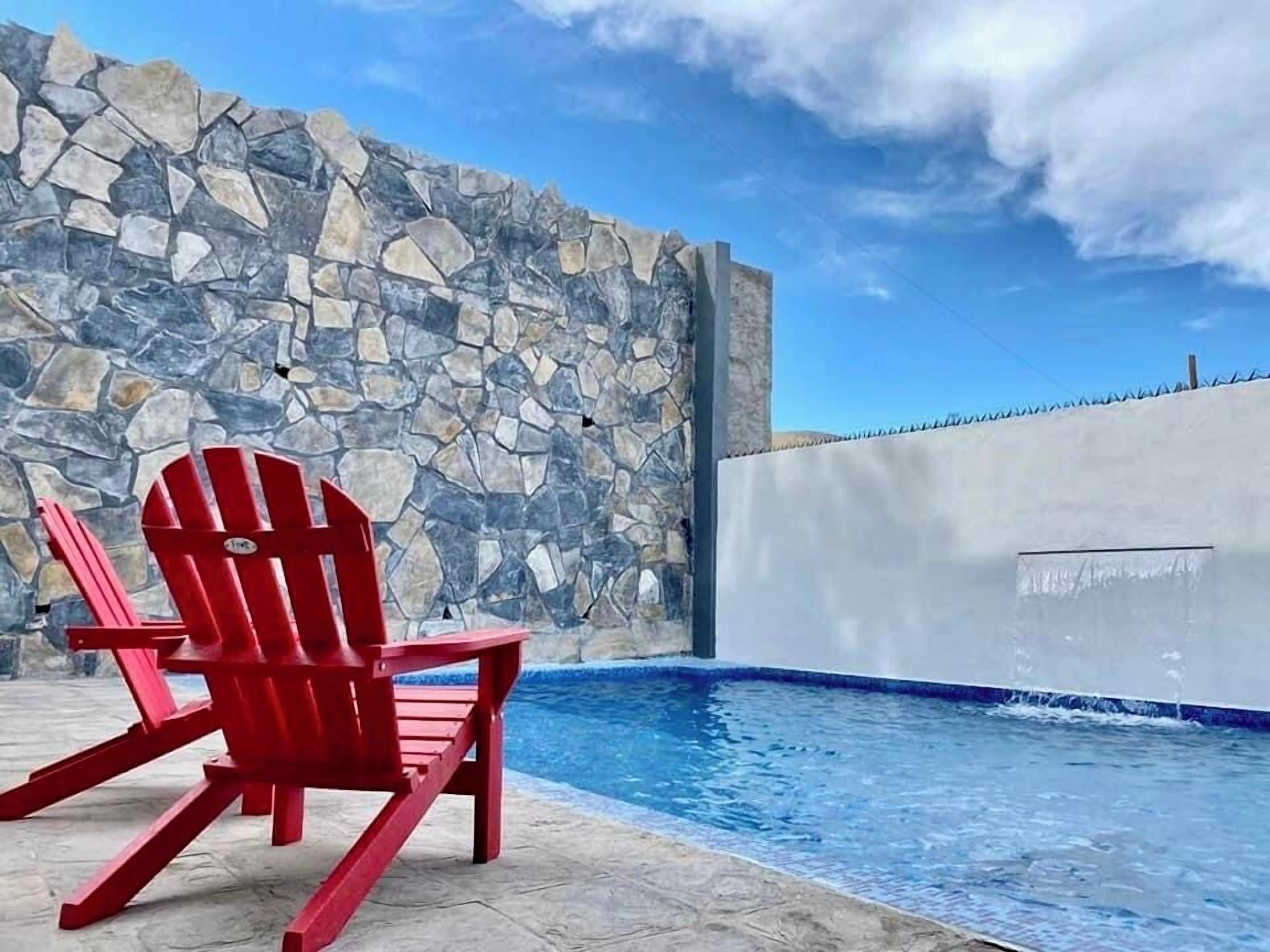 A red Adirondack chair by a stone wall and a pool with a blue edge.
