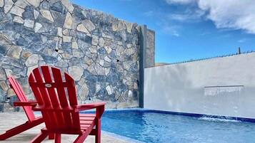 A red Adirondack chair by a stone wall and a pool with a blue edge.