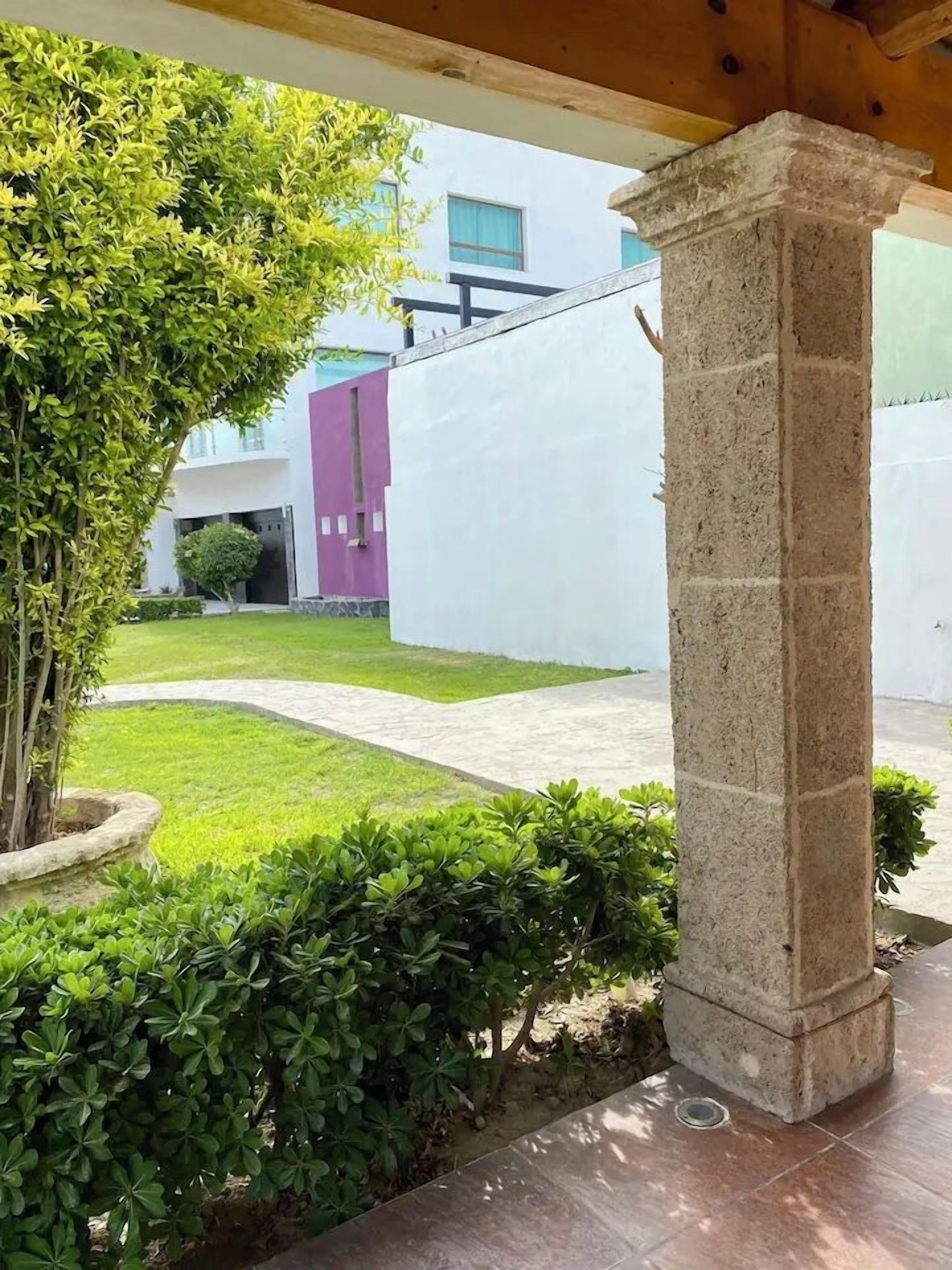 A courtyard with a stone column, a well-maintained lawn, and a building in the background.