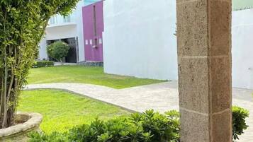 A courtyard with a stone column, a well-maintained lawn, and a building in the background.
