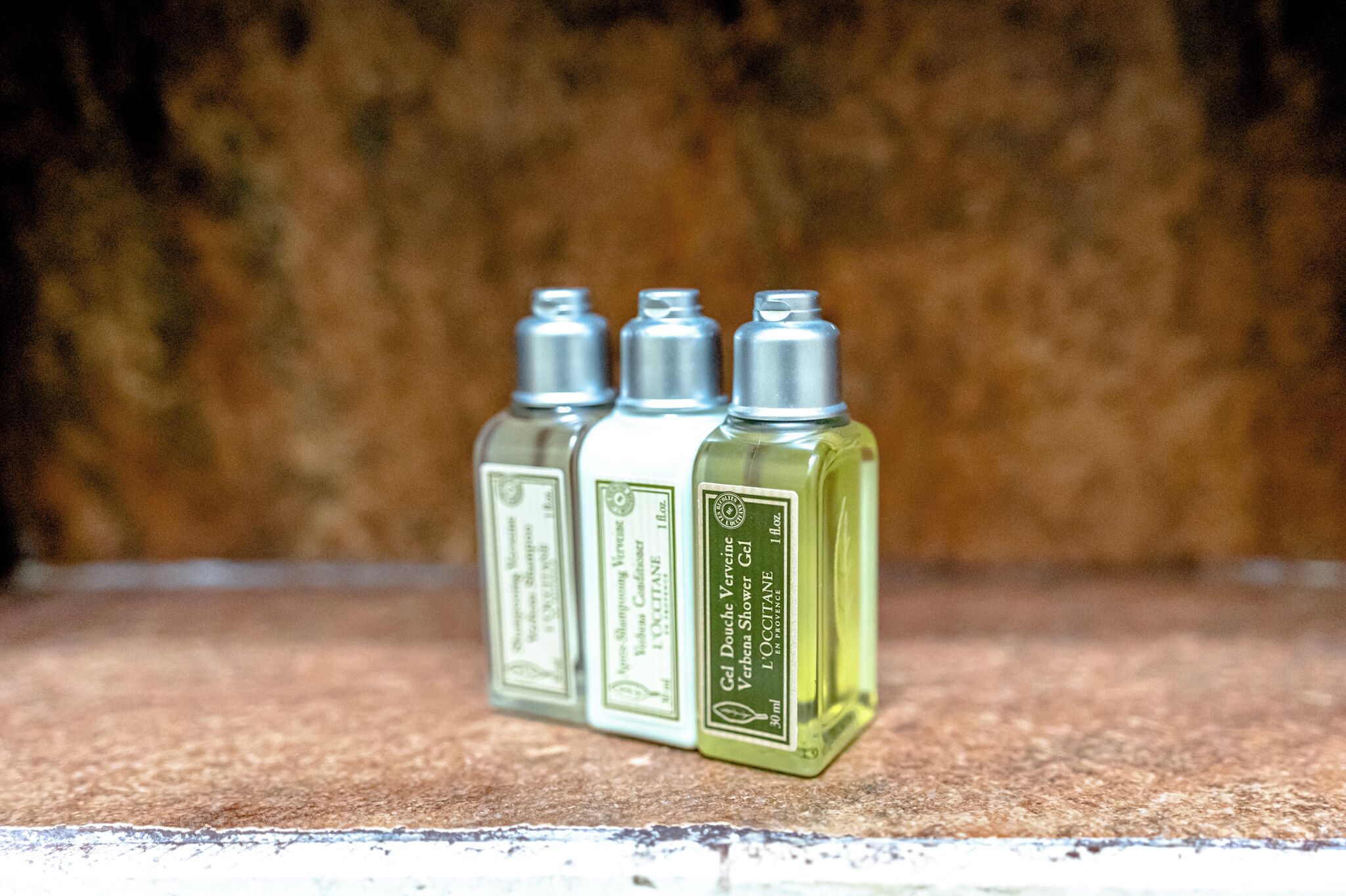 Three bottles of L'Occitane shower gel on a textured surface.