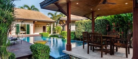 A poolside area with a wooden deck, outdoor furniture, and a covered seating area.