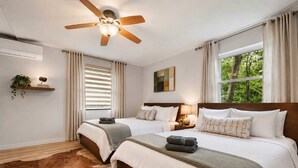 A bedroom with two beds, a ceiling fan, a window with curtains, a wooden floor, and a cowhide rug.