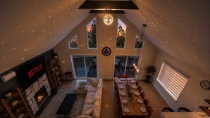 A loft-style living room with a fireplace, a dining area, and a large window overlooking a deck.