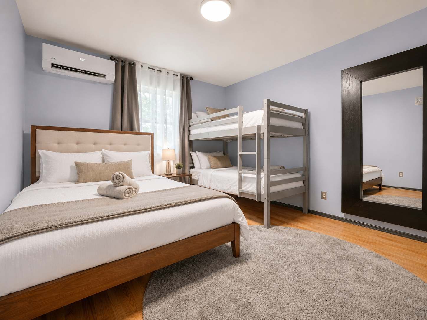 Een hotelkamer met een enkel bed, een stapelbed, een grote spiegel en een airconditioning.