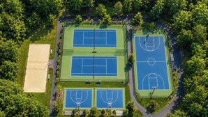 An aerial view of a sports complex with multiple tennis courts, a basketball court, and a sand court.