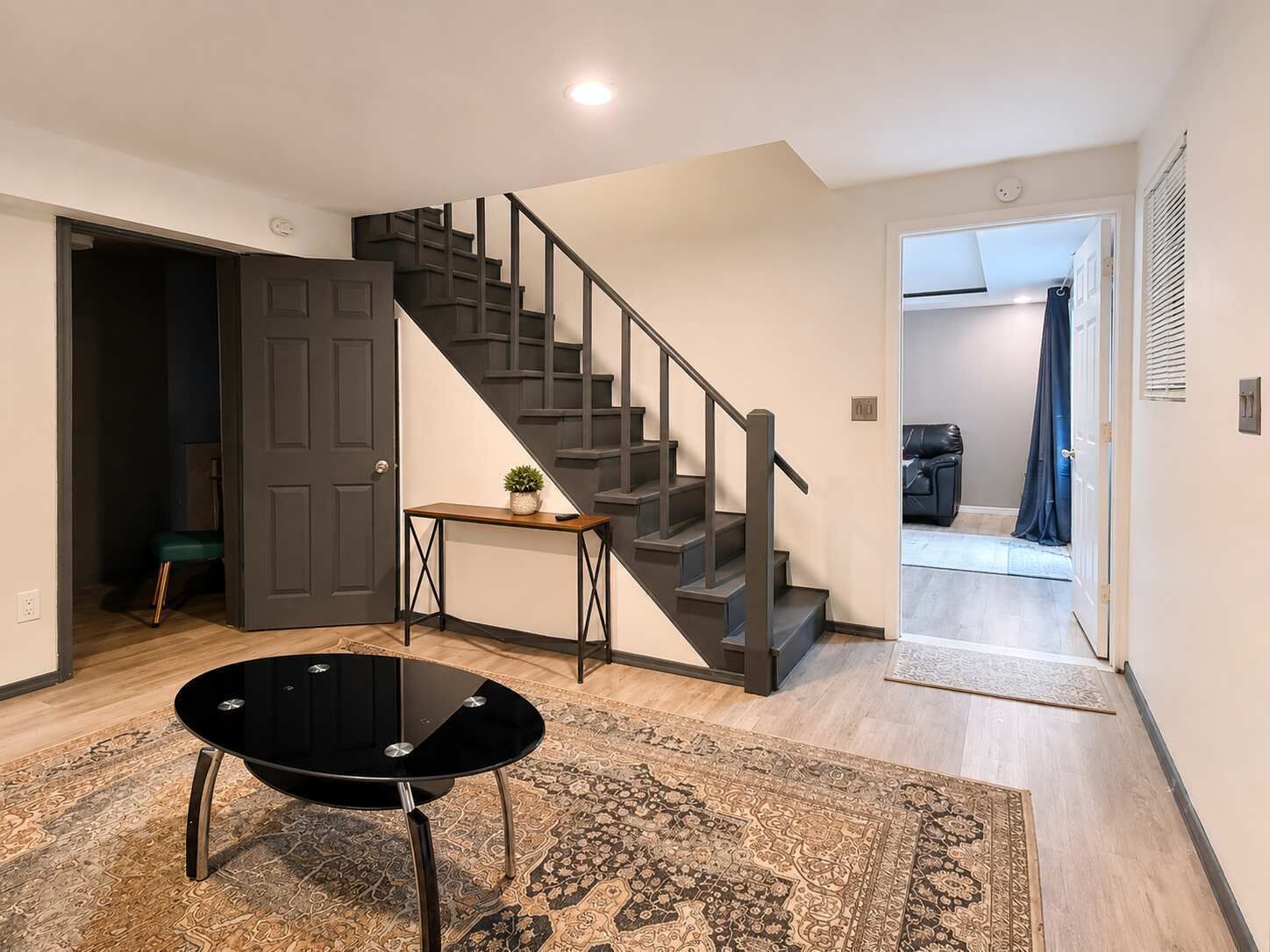 Un intérieur moderne avec un escalier, une petite table agrémentée d’une plante et une table noire aux pieds en métal.