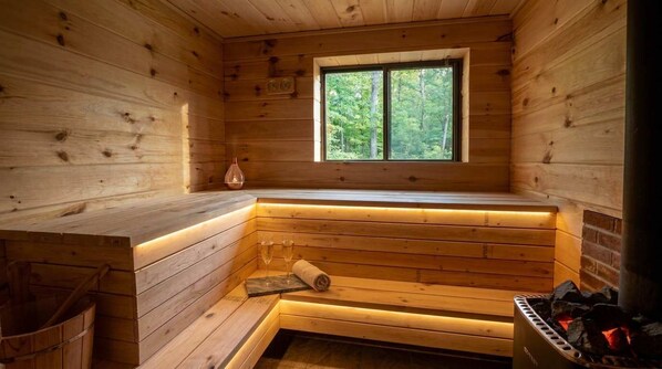 A wooden sauna with a bench, a window, and a visible fireplace.