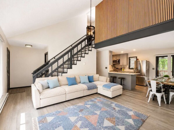Un espace de vie moderne comprenant un canapé d’angle, un escalier, une cuisine et un coin repas.