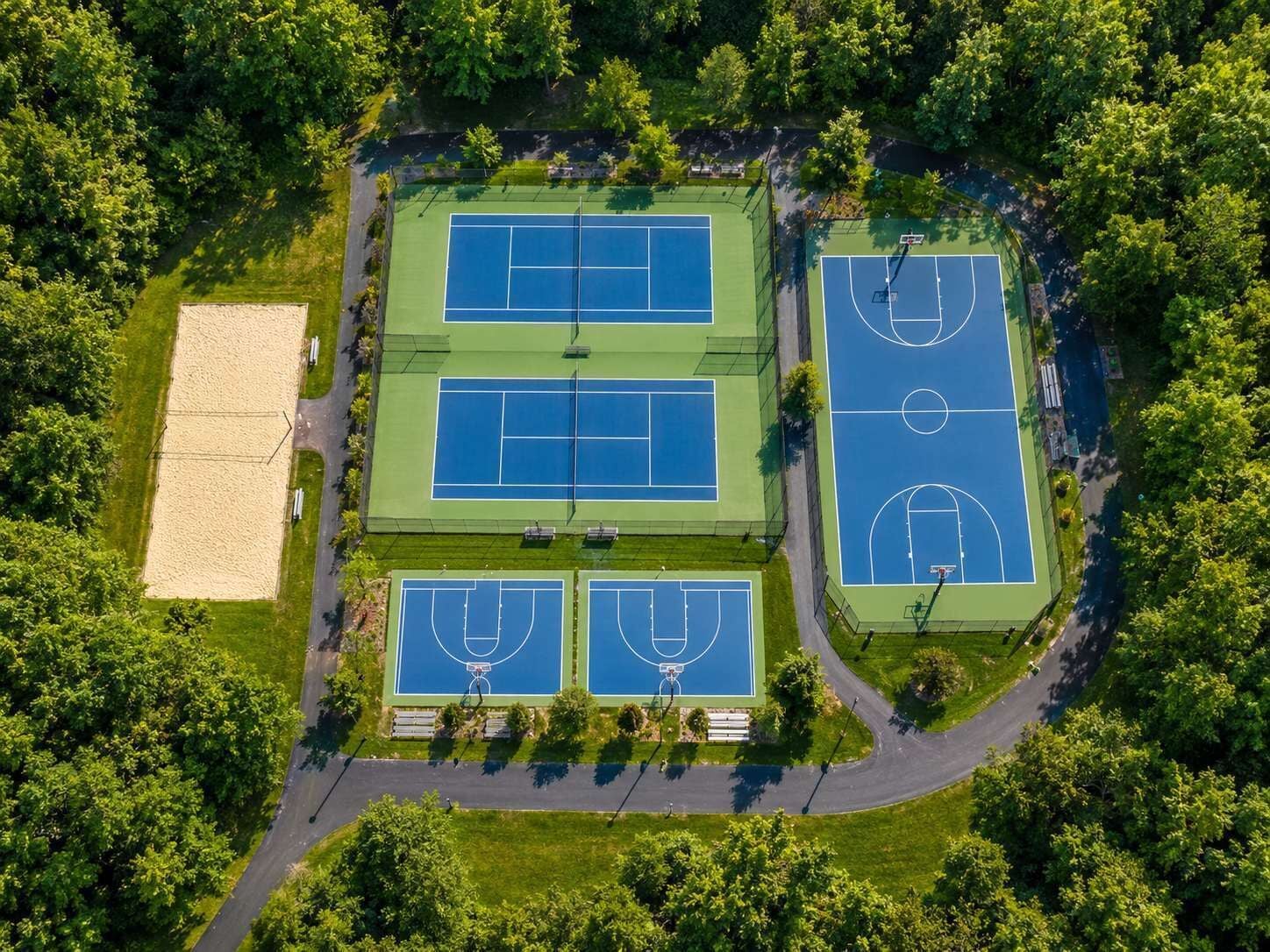 An aerial view of a sports complex with multiple tennis courts, a basketball court, and a sand court.