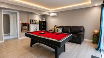 A modern living room with a pool table, a leather sofa, and a billiards rack.