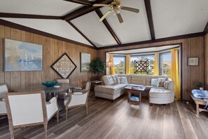 A spacious living room with a wooden ceiling, a large sofa, a dining table, and a view through a window. - 7648- QuinnaKeeters', Pet-Friendly Avon Cottage | 3 Min Walk to Surf (Avon)