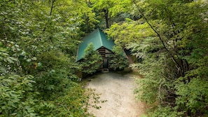 Una cabaña rodeada de un bosque denso con un camino de grava que lleva a ella.