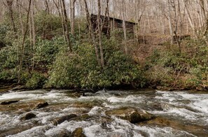 A river flowing through a forest with a rustic cabin in the background. - Cherokee Lodge-Pet Friendly, Luxury Log Cabin Rental, Hot Tub, 2 Fireplaces, Fishing- Nantahala NC. (Topton)
