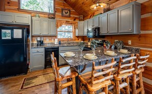 A kitchen with granite countertops, wooden chairs, and a black refrigerator.