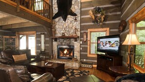 A log cabin interior with a stone fireplace, leather furniture, a television, and a balcony. - Water's Edge-Pet Friendly 3 Bedroom, Luxury Log Cabin Rental, Perfect for Families, Outdoor Entertaining, Hot Tub, Fireplace, 30 Minutes to Great Smoky Mountains-Nantahala NC (Topton)