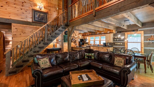 A cabin interior with a wooden staircase, leather sectional sofa, and a dining area. - Water's Edge-Pet Friendly 3 Bedroom, Luxury Log Cabin Rental, Perfect for Families, Outdoor Entertaining, Hot Tub, Fireplace, 30 Minutes to Great Smoky Mountains-Nantahala NC (Topton)
