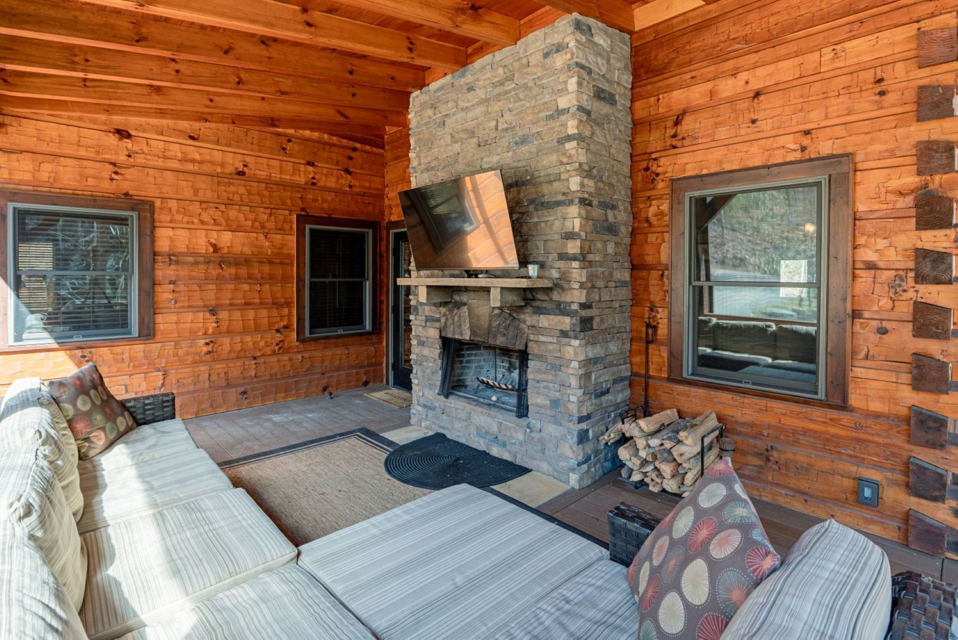 Ein Holzblockhaus-Interieur mit Kamin aus Stein, einer Couch und zwei Fenstern.