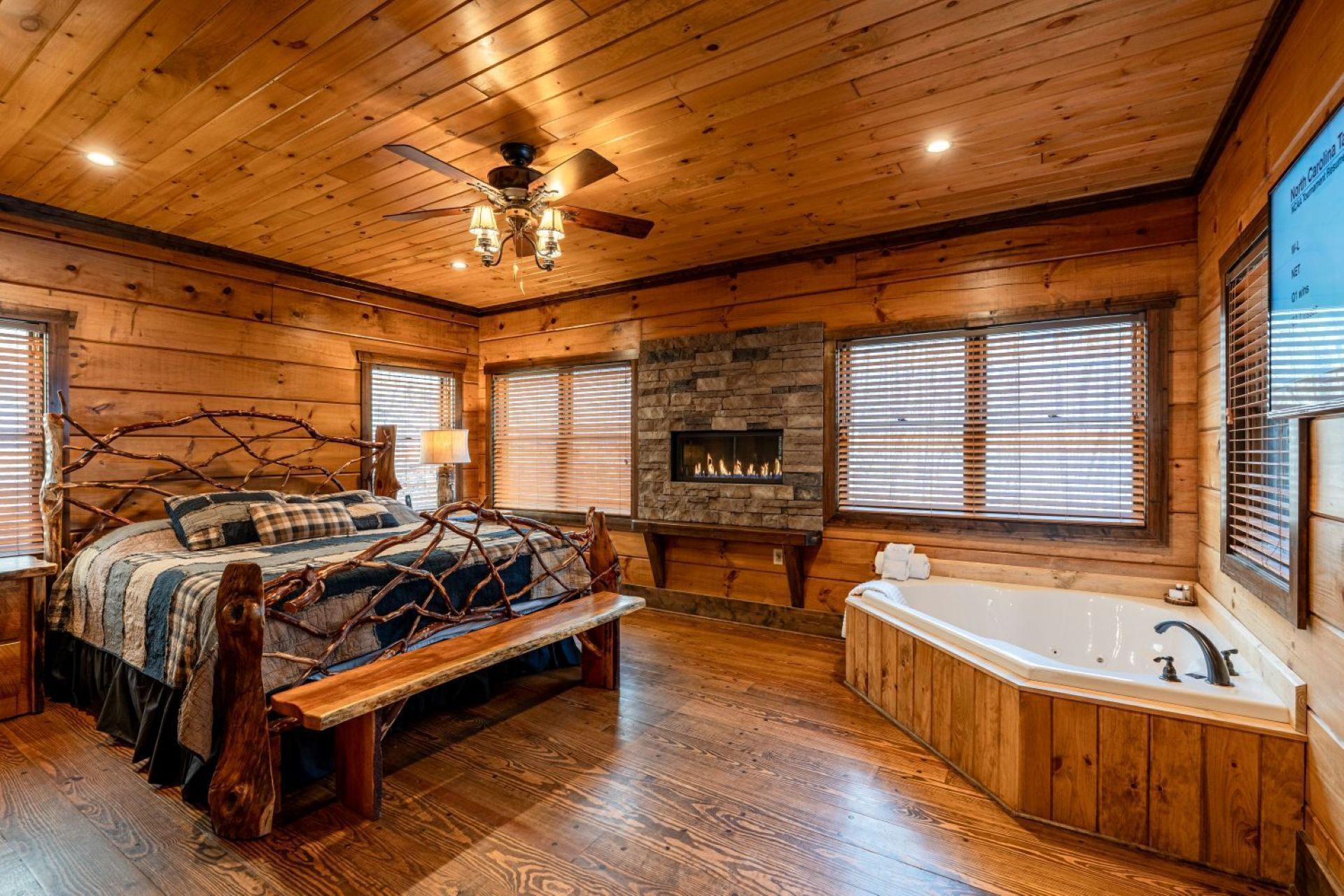 A log cabin interior with a bed, a fireplace, a bathtub, and a ceiling fan.