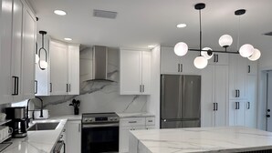 Cocina moderna con muebles blancos, una isla grande con asientos, electrodomésticos de acero inoxidable y salpicadero de mármol.