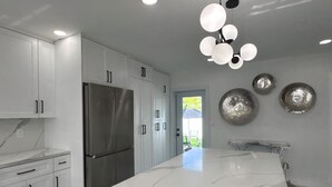Una cocina moderna con armarios blancos, un refrigerador de acero inoxidable, una isla de mármol y una lámpara de techo original.