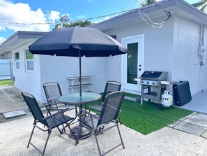 A patio with a round table and chairs, a grill, and a gas cylinder.
