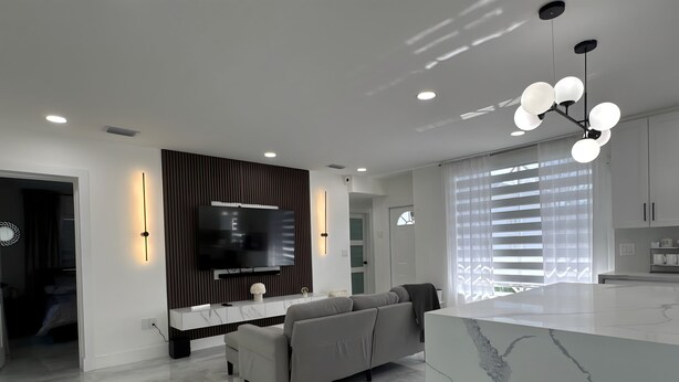 Una sala de estar moderna con un televisor grande, un sofá, una isla de mármol y un comedor con una cocina al fondo.
