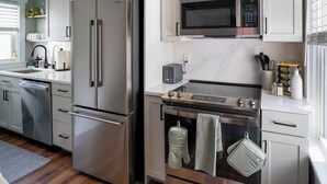 A modern kitchen with stainless steel appliances, white cabinetry, and a marble backsplash. - Stylish Apt Walk to Shops, Dining and Bucknell (Lewisburg)