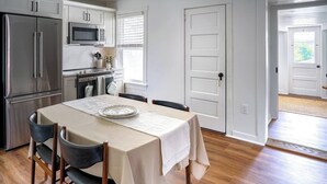 A modern kitchen with stainless steel appliances, a dining table with chairs, and a view of the outside through a door. - Stylish Apt Walk to Shops, Dining and Bucknell (Lewisburg)