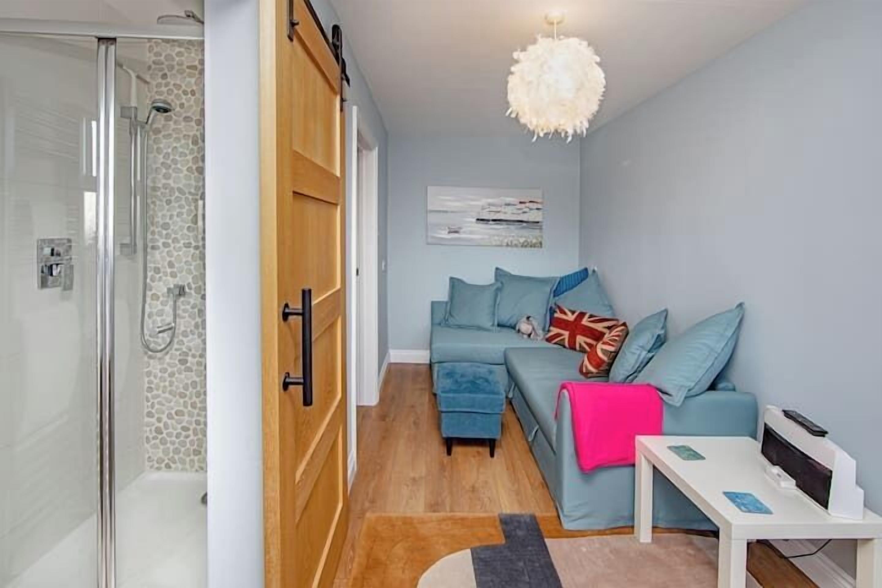 A modern living room with a glass shower enclosure, a wooden wardrobe, a blue sofa with cushions, and a white table with a printer.