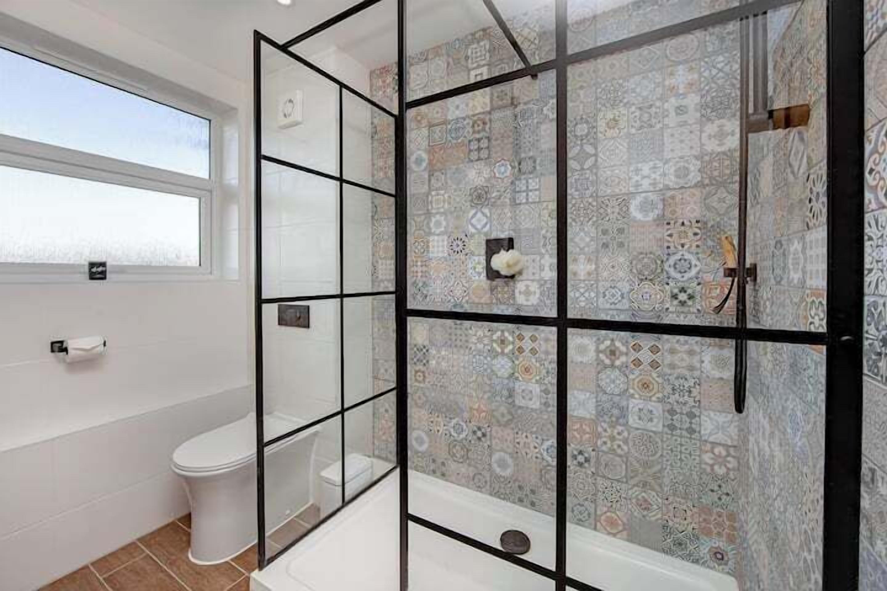 A bathroom with a glass partition, a toilet, a bathtub, and a shower area with patterned tiles.