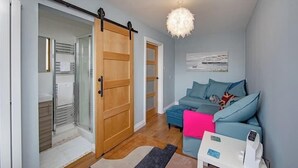 A modern living room with a sliding door, a blue sofa, a white coffee table, and a chandelier. - Coastal Charm In Clacton On Sea / With Balcony & Sea View / Sleeps 4 (Essex)